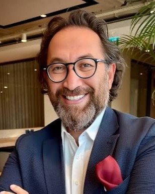 AIx Leadership Bootcamp eğitmeni Kadir Ceran, bir toplantı salonunda gülümserken.